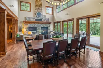 Upon entry, a breathtaking great room soars two stories high, featuring exposed beams, a floor-to-ceiling stone fireplace, and a striking wall of glass doors and upper windows that flood the space with natural light and scenic views.