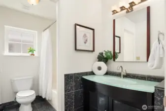 The main bath is large with a linen closet (unseen to the left) and a designer vanity as well as extensive tile work and a full bathtub.