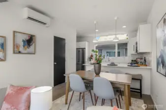 As we continue through the main level, you'll notice how the elevated ceilings create a sense of scale, comfortably accommodating both a full-sized dining table and a functional breakfast bar. The expansive windows flood the space with natural light, while the discreet door to the left provides practical understairs storage.