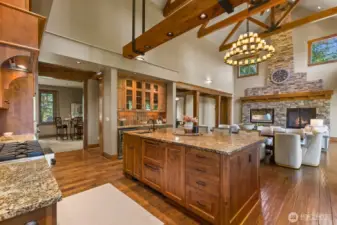 Gourmet kitchen features complimentary china cabinet, beverage cooler, and chef-grade refrigerator seamlessly integrated into a slab-granite island with power outlets, framed by custom knotty pine cabinetry.