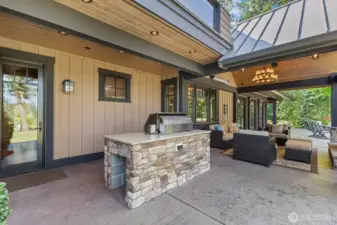 Refined outdoor living area featuring Viking BBQ, heated entertainment patio, and nearby restroom and garage entry, all set amid beautifully maintained gardens and open green views.