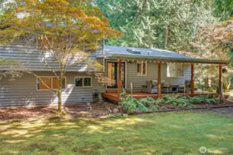 From the backyard, the home’s covered deck extends the living space outdoors. Surrounded by trees, this area blends indoor comfort with the beauty of nature.