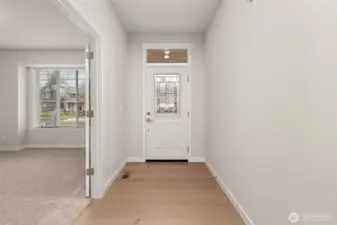 Looking toward the front door. The front door is white with a decorative glass insert and a transom window above, allowing natural light to filter in.