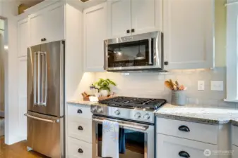 Stainless steel appliances, a classic subway tile backsplash, undercounter lighting, and pull-out cabinet drawers blend style with everyday function. The pantry to the left of the refrigerator provides additional storage, too.