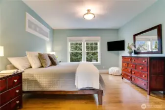 Natural light pours through the wood-wrapped windows, framed by views of lush, tranquil trees. Hardwood floors and refined window coverings add warmth and sophistication.