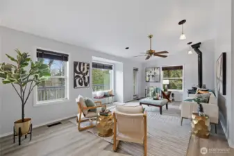 Sun-soaked living room features new flooring, soaring ceilings, and wall-to-wall windows framing treetop views.