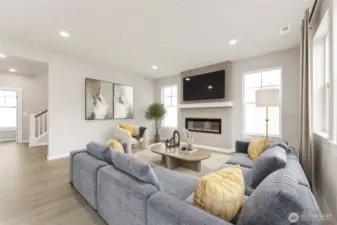 Open concept great room surrounded by windows and modern fireplace. Virtual staging in photo.