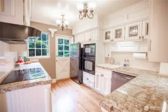 A modern kitchen outfitted with stainless appliances, white cabinetry and slabs of granite on the countertops.