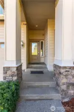 Welcome to your new home! The covered front entry makes a warm first impression with stone accents, clean lines, and a modern craftsman design. The sheltered walkway adds charm and practicality—perfect for greeting guests or staying dry on a rainy Washington day. A glass front door lets natural light into the foyer, giving a glimpse of the bright, welcoming space inside.