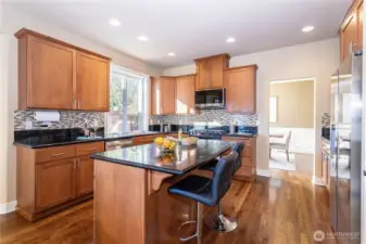 Modern kitchen featuring solid wood cabinetry, a central island with bar seating, and sleek granite counters. Stainless-steel appliances and tile backsplash elevate the design, offering both beauty and function.