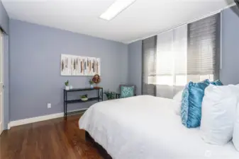 This secondary bedroom combines cool blue walls with crisp white trim and hardwood floors for a refreshing, modern touch. Oversized windows allow for plenty of daylight, while built-in shelving and generous space make it perfect for guests or a secondary suite setup.
