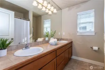 Stylish full bath featuring dual sinks, wide vanity, and tile countertops. A full-size tub and shower combination, soft lighting, and natural-toned finishes create a clean, relaxing atmosphere. Perfectly located to serve the upstairs bedrooms and loft.