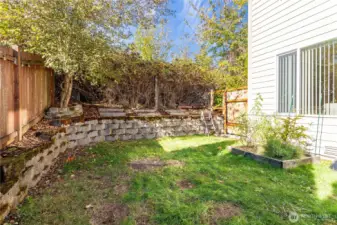 Private, fully fenced backyard with raised garden beds and terraced landscaping framed by mature trees. A great balance of low maintenance and opportunity to personalize—perfect for gardening or relaxing in the sunshine.