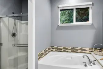 Oval soaking tub with Mosaic glass tile accented backsplash and Quartz counter and window above with two-inch blinds and screen. Paneled Quaker pocket door to watercloset and shower privacy room. Elongated watercloset. Step-in shower with glass doors, handheld shower wand.