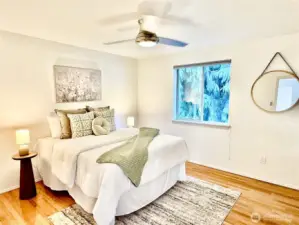 Bright and airy bedroom with beautiful hardwood floors, a ceiling fan, and large windows overlooking mature landscaping.