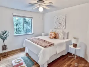 Comfortable secondary bedroom with hardwood flooring, a ceiling fan, and treed view. Perfect for family or guests.