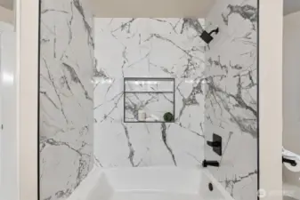 Full bath with marble-style surround and niche shelving detail.