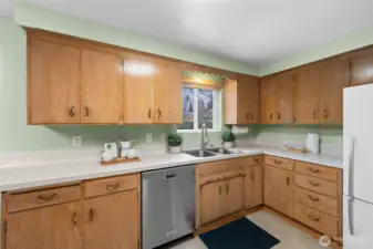 Double-basin sink positioned beneath the window brings natural light into the workspace. Stainless dishwasher and surrounding cabinetry keep everyday essentials within easy reach.