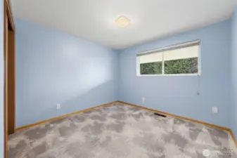Bedroom Two with calming wall color and an updated vinyl window that brings in daylight and outdoor views. Carpet covers original hardwood floors, offering flexibility for future design choices.