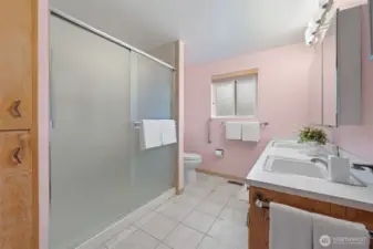 Main bathroom features a spacious walk-in shower with sliding glass doors and a wide vanity with dual sinks for everyday convenience. A frosted window provides natural light and privacy, while the generous layout offers comfortable room to move.