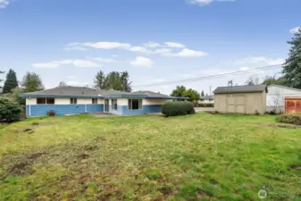 Expansive backyard offers a wide lawn with plenty of room for outdoor activities, gardening, or future landscaping ideas. A detached storage shed adds convenient space for tools and equipment.