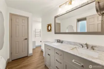 Primary suite bathroom vanity with dual inset  sinks and large horizontal mirror. Around the corner is towel rack, shower/tub and linen  closet space. Behind closed door houses the  toilet for extra privacy.