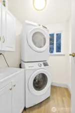 Laundry room to the right as you walk in main home entrance next to stairway to primary suite. Stacked Washer & Dryer to conserve space, storage for laundry and cleaning supplies, and Luxury Vinyl Plank flooring for easy cleaning.