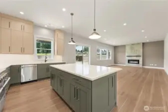 Bright and open-concept kitchen flows seamlessly into the spacious living area, anchored by a sleek modern fireplace. Expansive windows and glass doors fill the space with natural light, while the oversized island with waterfall countertops offers the perfect spot for casual meals, prep, and entertaining.