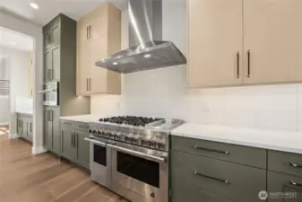 Chef-worthy kitchen with a professional-grade gas range, sleek stainless steel hood, and full tile backsplash. The modern two-tone cabinetry offers generous storage and striking contrast, complemented by elegant quartz counters and matte black hardware.
