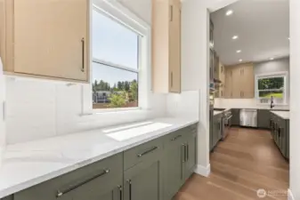 A bright and airy butler’s pantry offers additional prep and storage space with matching quartz countertops, modern cabinetry, and serene views through the window—seamlessly connected to the main kitchen for effortless flow.
