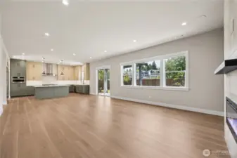 Spacious open-concept layout with wide-plank flooring, large windows, and seamless flow from kitchen to living area. A modern gas fireplace adds warmth and style.