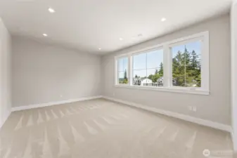 Spacious upstairs bedroom with plush carpet, recessed lighting, and a wall of windows offering treetop views and natural light.