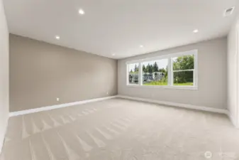 Expansive primary suite with plush carpet, soft accent wall, and oversized windows offering serene greenbelt views.