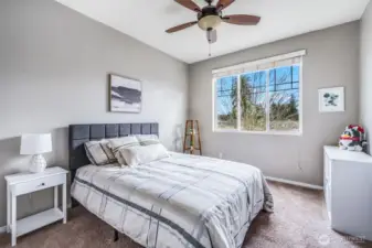 This bright and inviting bedroom features plush carpeting, a stylish ceiling fan, and a large window that fills the space with natural light, creating a cozy and comfortable retreat.