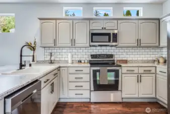 This beautifully designed kitchen features stainless steel appliances, a classic subway tile backsplash, rich laminate wood flooring, and a stylish gooseneck faucet—blending elegance and functionality for effortless cooking and entertaining.