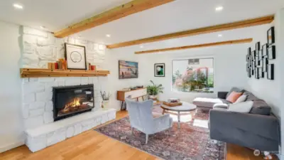 Beautifully updated living room with wood beams, large window, recessed lighting and cozy fireplace with wooden mantel.