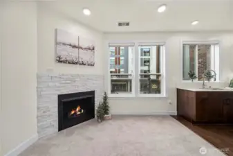 The living room features a modern gas fireplace with a stacked-stone surround, creating a warm focal point for the space. Large windows bring in generous natural light and offer views of the vibrant Point Ruston community below.