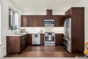 A spacious kitchen featuring rich wood cabinetry, sleek quartz counters, and premium stainless steel appliances. The clean design and ample storage make meal prep effortless while maintaining a modern, streamlined look.