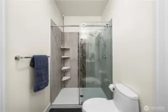 This updated 3/4 bath features a sleek glass-enclosed shower with floor-to-ceiling tile and an accent mosaic strip for added style. Built-in corner shelving provides convenient storage, while the neutral finishes keep the space bright and modern.