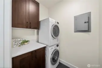 The dedicated laundry room offers practical convenience with a stacked washer and dryer, overhead cabinetry, and a spacious countertop for folding or storage. Thoughtful design makes everyday routines easier while keeping the home organized.