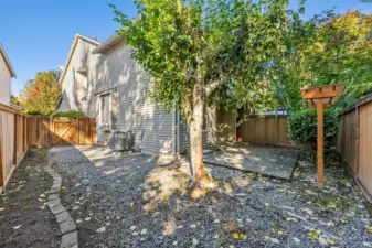From far back corner of backyard, side gate access, gravel ground covering with separated garden space. Trellis located in front of back fence line for growing crawling plants.
