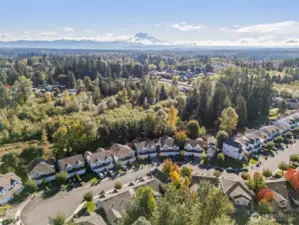 Aerial view of community at end of cul-de-sac with Mt Rainier in the backdrop. Greenbelt on the back-edge of community where townhouse unit is located.