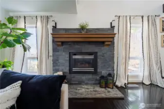 A gorgeous gas fireplace with a stacked stone surround, solid stone hearth, and timeless wood mantle