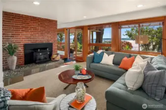 The lower-level family room with brick fireplace, large wood windows, framing those water views and seamless access to the patio, perfect for gathering and relaxation.