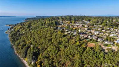 This aerial view highlights the home’s stunning bluff-top location in the Arroyos, showcasing both the expansive Puget Sound coastline and the surrounding forested landscape - with the Seattle skyline visible in the distance.