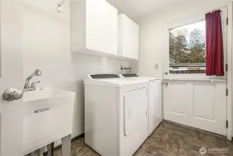 Laundry room with utility sink, storage, and charming farmhouse-style door to backyard.