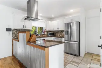 Custom corrugated metal adds a unique industrial touch, while the mosaic tile backsplash ties the space together beautifully~