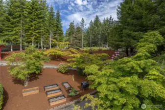 Beautifully maintained gardens with native rhododendrons, flowering trees, and raised beds ready for vegetables and herbs.