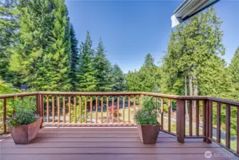 A view of the west-facing, water-resistant deck off of the primary bedroom. The deck overlooks the gardens and on clear days the Olympics peak out over the trees.