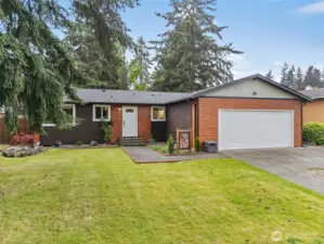 Another angle of the front exterior, showcasing the wide driveway, manicured lawn, and mature trees that add character and shade.